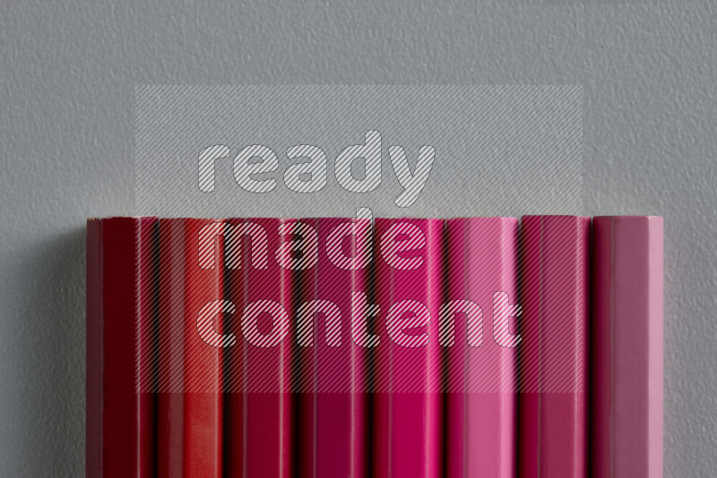 A collection of colored pencils arranged showcasing a gradient of pink and red hues on grey background