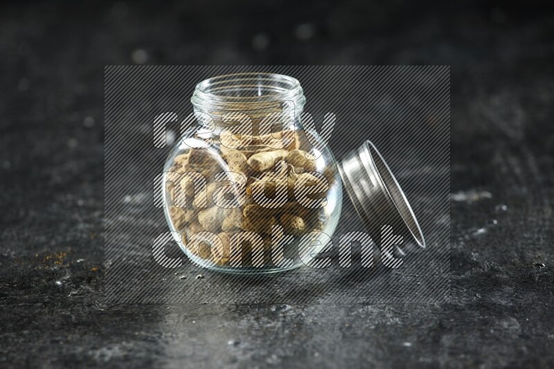 A glass spice jar full of dried turmeric whole fingers on a textured black flooring