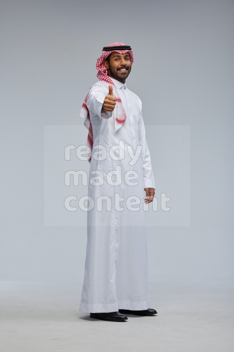 Saudi man Wearing Thob and shomag standing interacting with the camera on Gray background