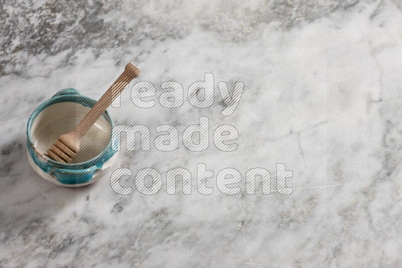 Multicolored pottery bowl with wooden honey dipper in it on grey marble background