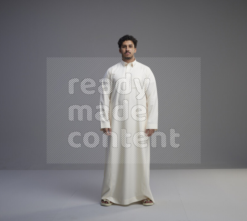 A Saudi man standing wearing thob interacting with the camera on gray background