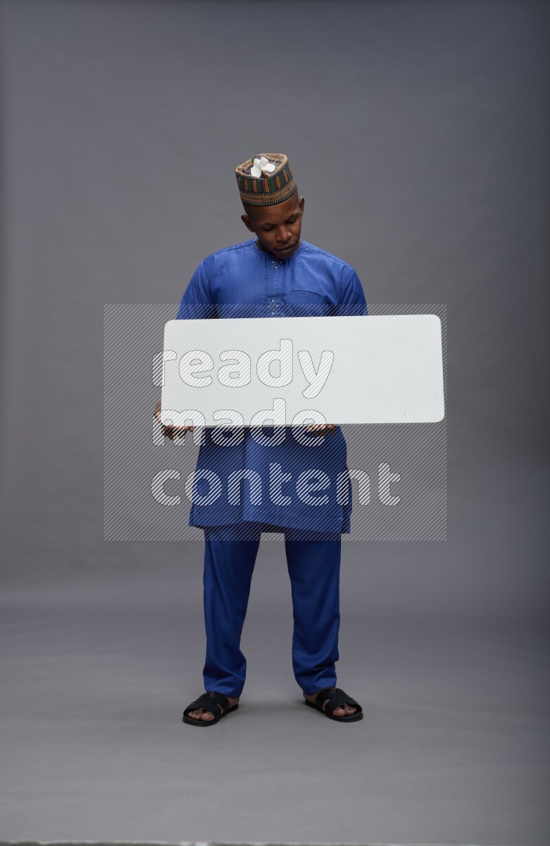 Man wearing Nigerian outfit standing holding board on gray background
