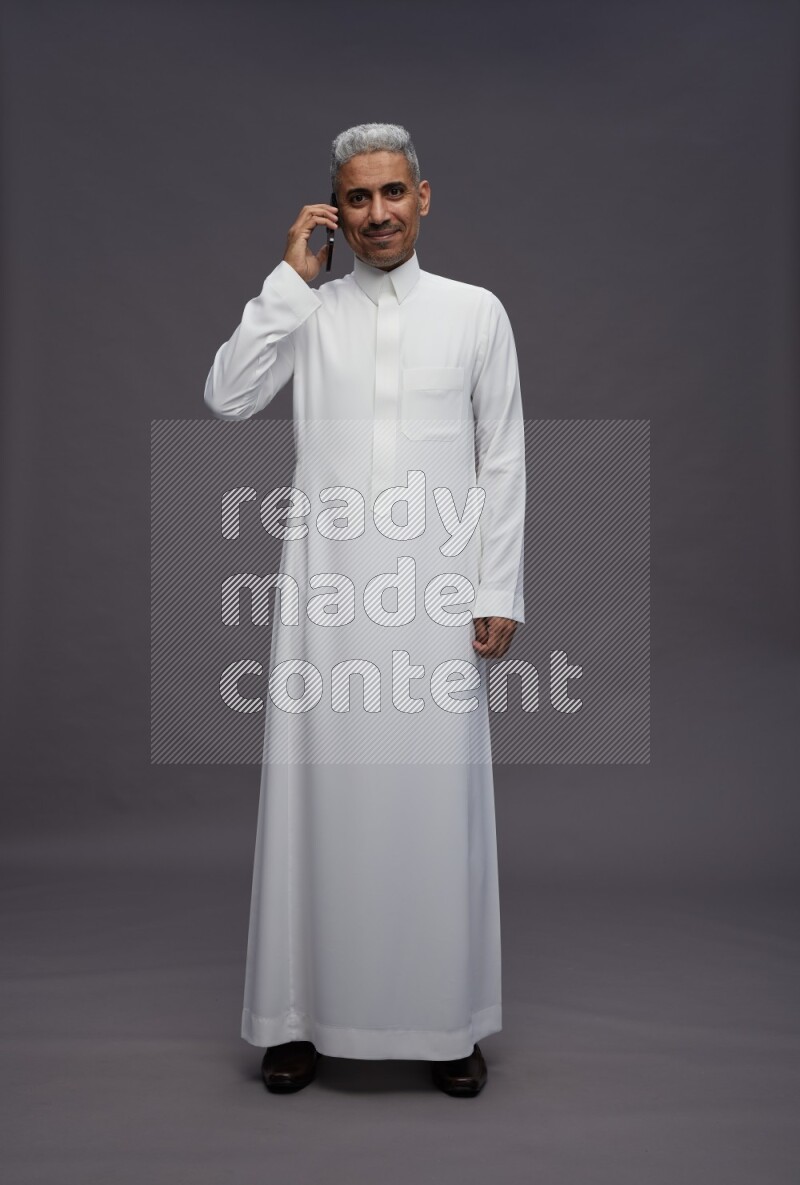 Saudi man wearing thob standing talking on phone on gray background