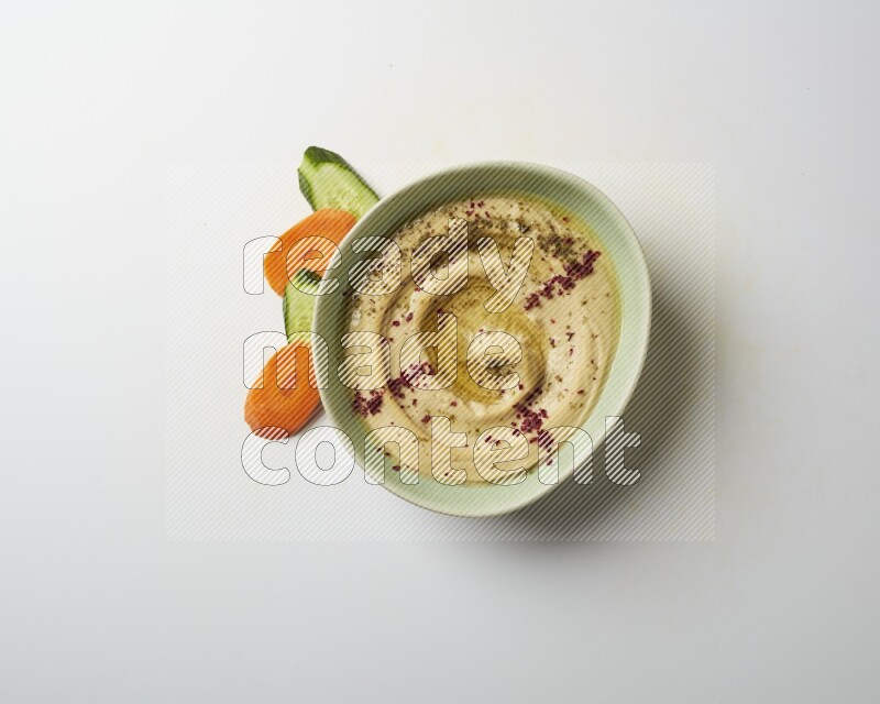 Hummus in a green plate garnished with zattar & sumak on a white background