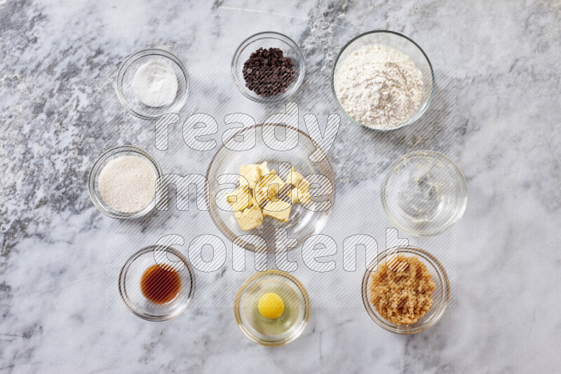 Cookies step by step with its ingredient, flour, butter, brown sugar, egg, vanilla extract, white sugar, chocolate chips and baking soda on grey marble background