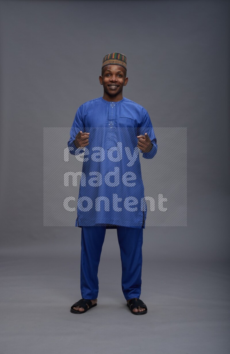 Man wearing Nigerian outfit standing interacting with the camera on gray background