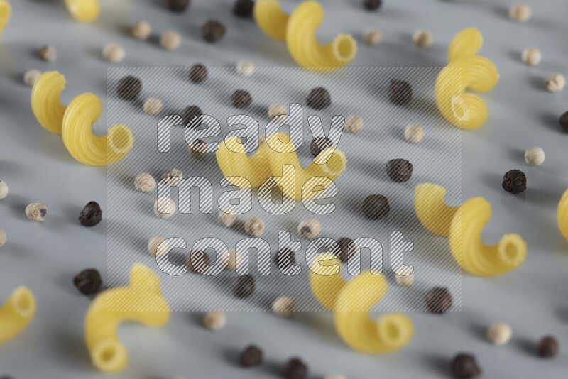Raw pasta with different ingredients such as cherry tomatoes, garlic, onions, red chilis, black pepper, white pepper, bay laurel leaves, rosemary, cardamom and mushrooms on light blue background