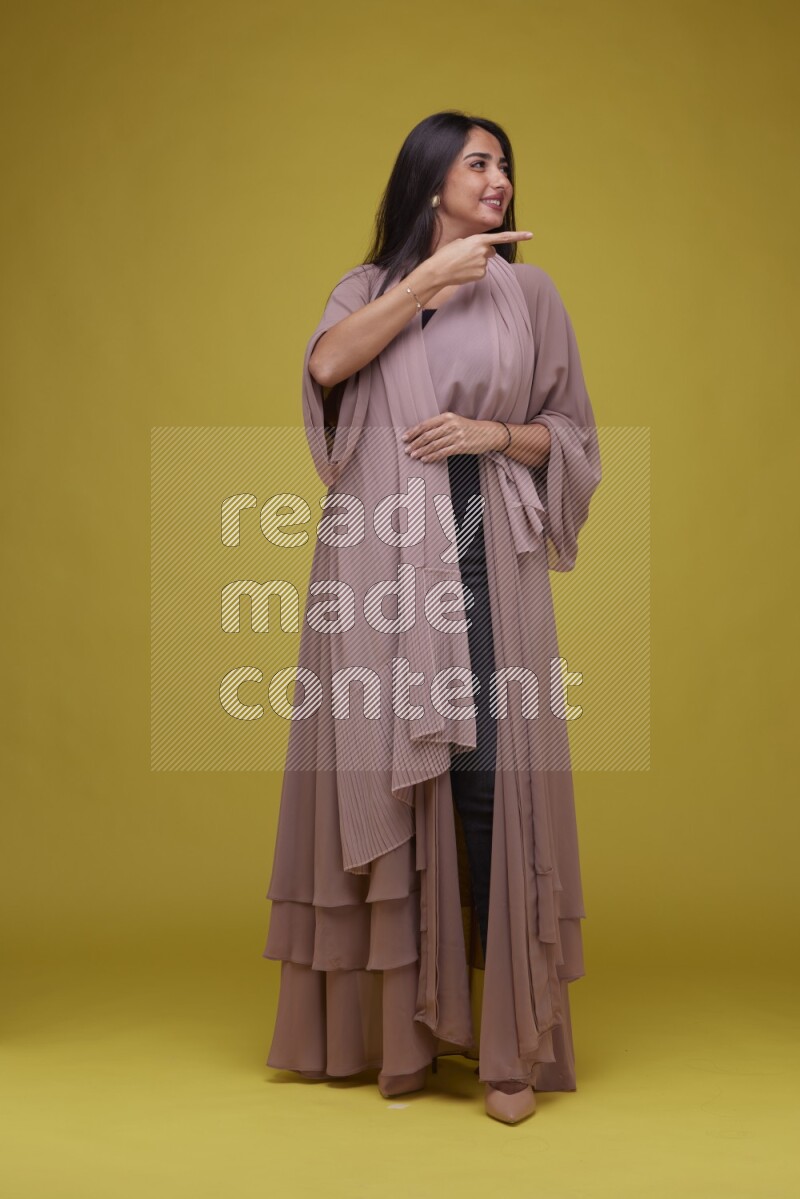 A woman Pointing on a Yellow Background wearing Brown Abaya