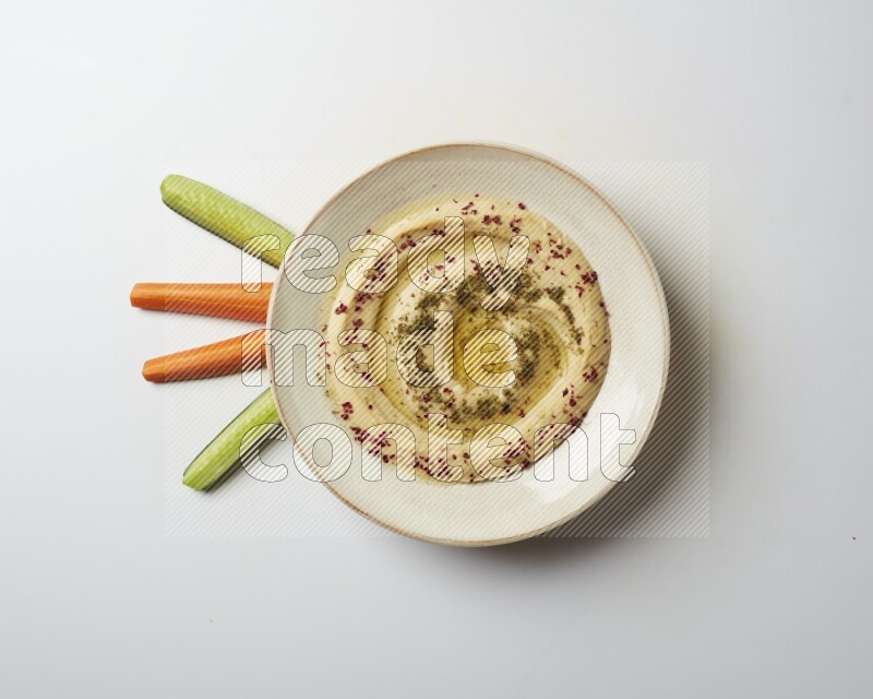 Hummus in a pottry plate garnished with zaatr & sumak on a white background