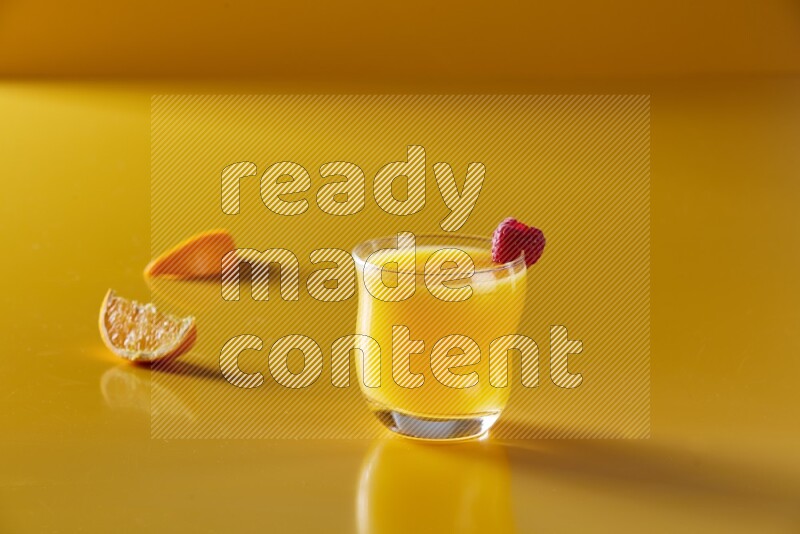 glass of orange juice with berry on yellow background