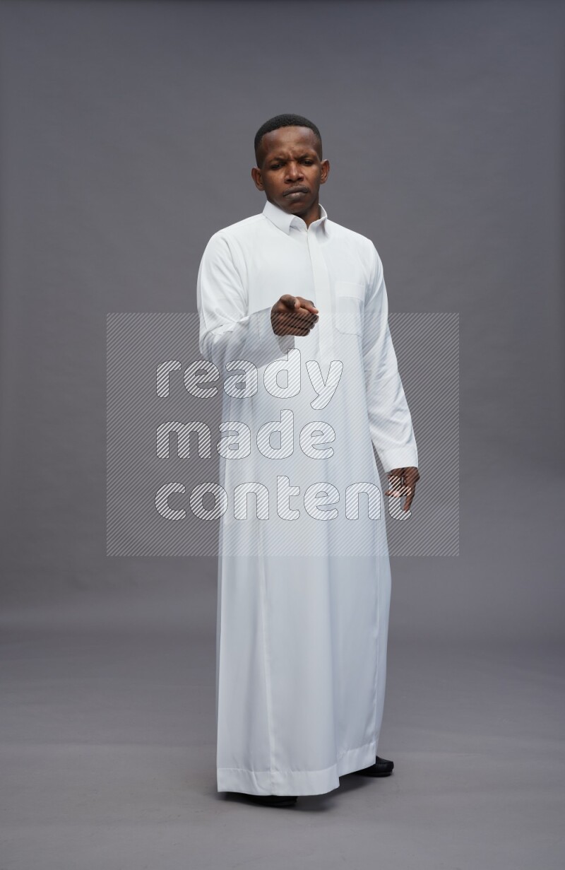 Saudi man wearing thob standing interacting with the camera on gray background