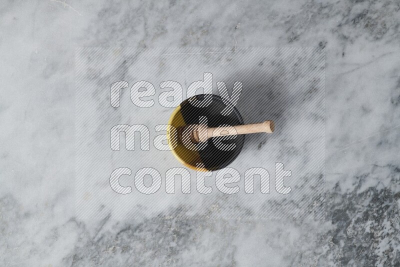 Multicolored pottery bowl with wooden honey dipper in it on grey marble background