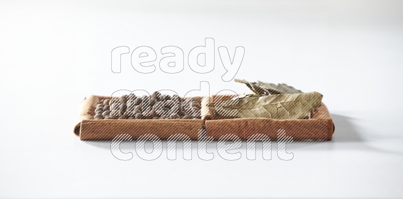 مربعان من أعواد القرفة ممتلئان ببهار الفلفل الحلو وأوراق الغار علي خلفية بيضاء