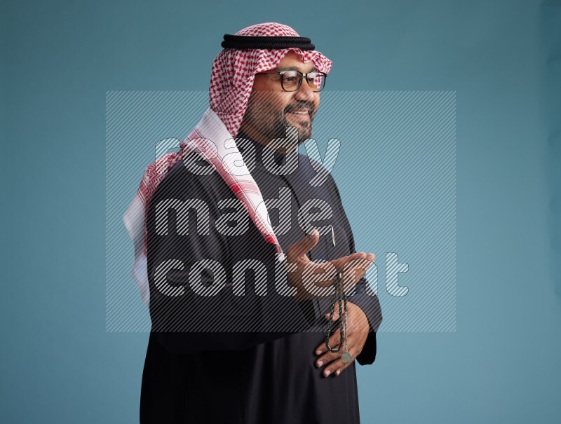 Saudi Man with shimag Standing Interacting with the camera on blue background