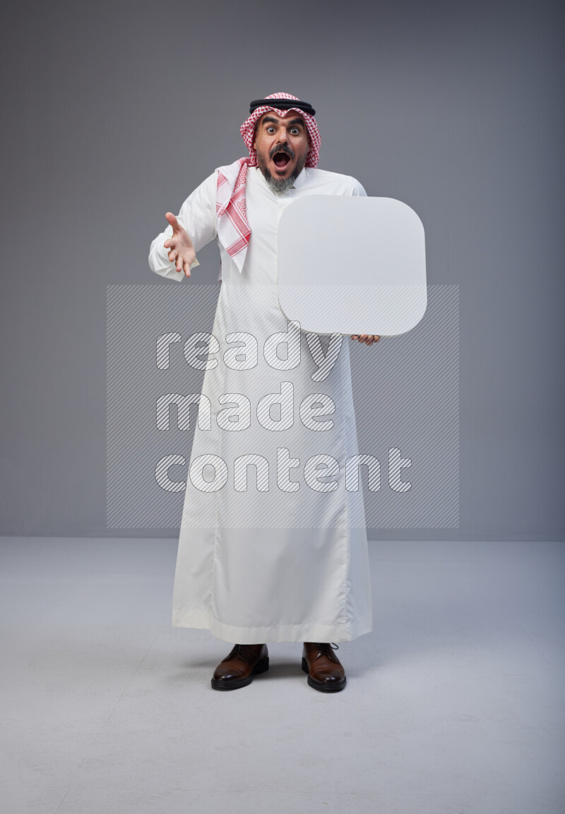 Saudi man Wearing Thob and red Shomag standing holding social media sign on Gray background