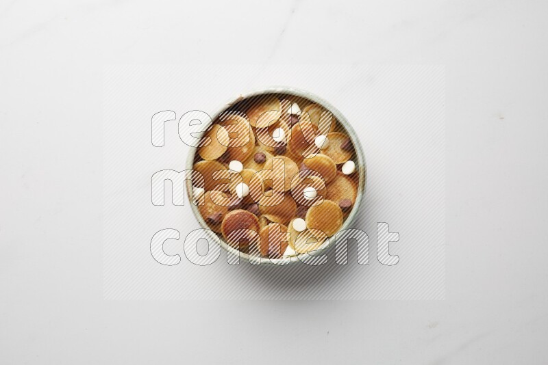 Top-view shot of mixed chocolate chips cereal pancakes in a round bowl on white background