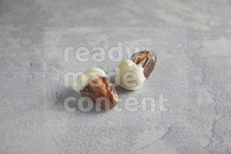 two almonds stuffed dates covered with white chololate on a light grey background