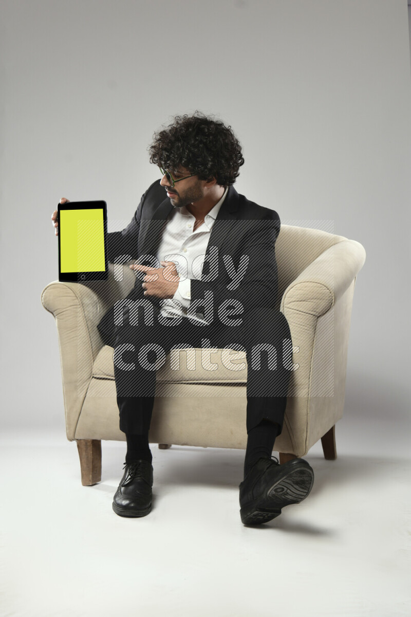 A man wearing formal sitting on a chair showing a tablet screen on white background