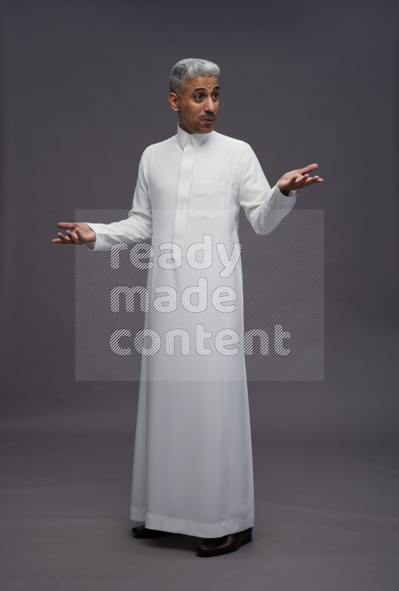 Saudi man wearing thob standing interacting with the camera on gray background