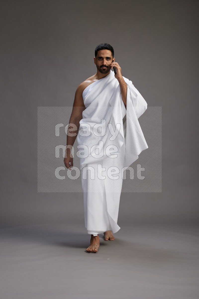 A man wearing Ehram Standing talking on phone on gray background