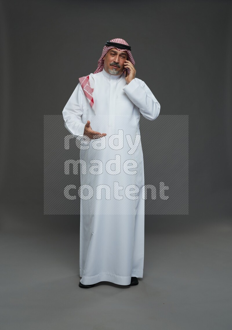 Saudi man with shomag Standing talking on phone on gray background