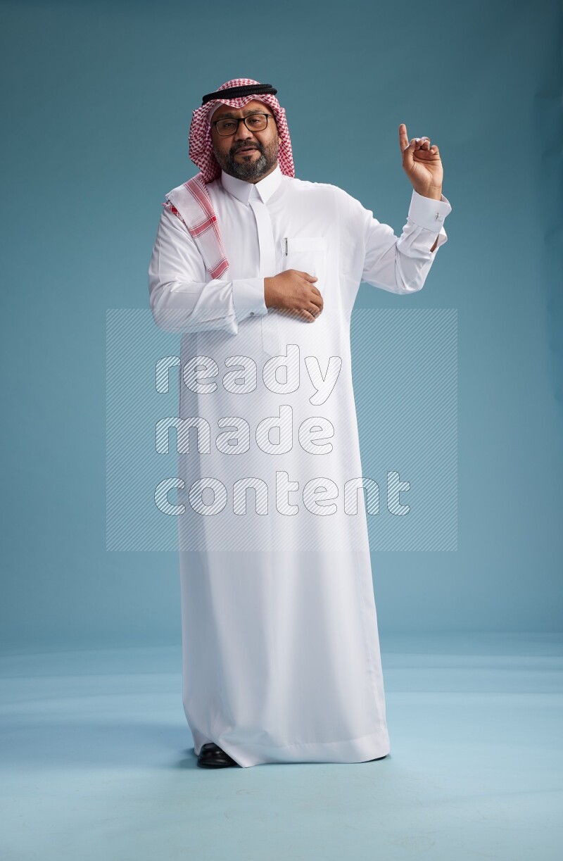 Saudi Man with shimag Standing Interacting with the camera on blue background
