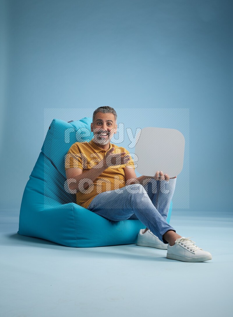 A man sitting on a blue beanbag and holding social media sign