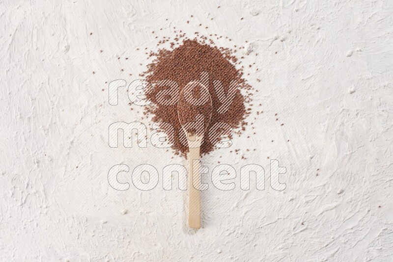 A wooden spoon full of garden cress seeds on a textured white flooring