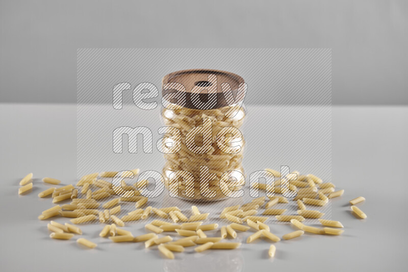 Raw pasta in a glass jar on light grey background