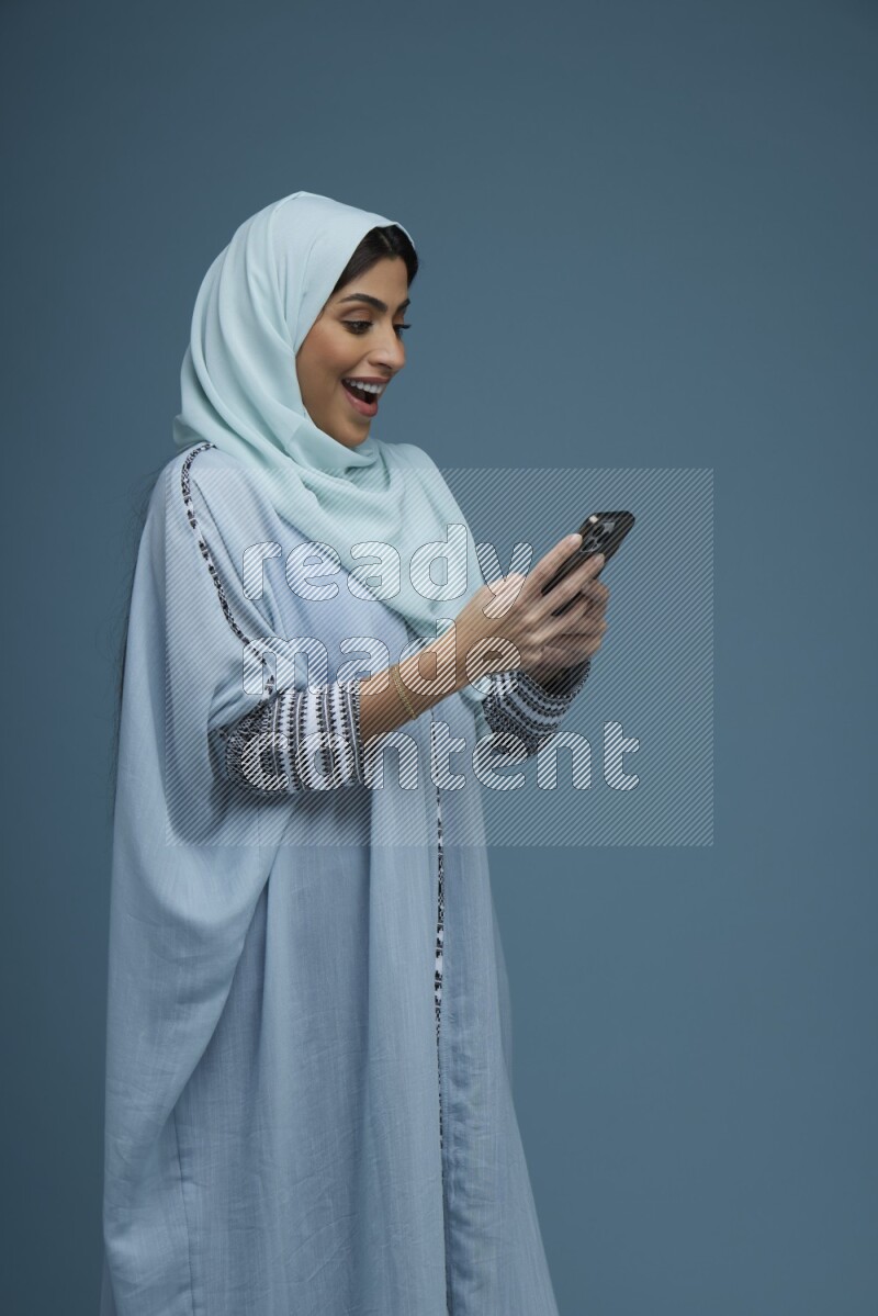 A Saudi woman Texting in a blue background wearing a blue Abaya with hijab