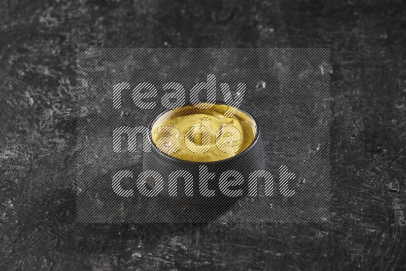 A black pottery bowl full of mustard paste on textured black flooring