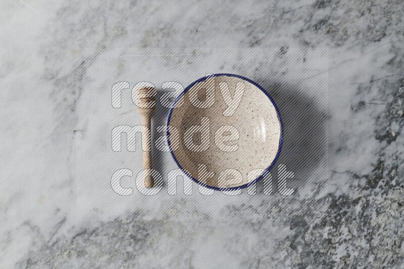 Multicolored pottery bowl with wooden honey dipper on the side on grey marble background