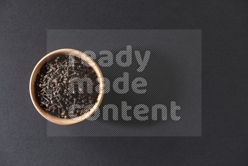 A wooden bowl full of cloves on a black flooring