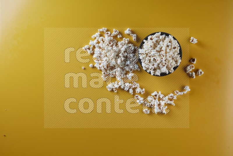 A black ceramic bowl full of popcorn with popcorn beside it on a yellow background in different angles