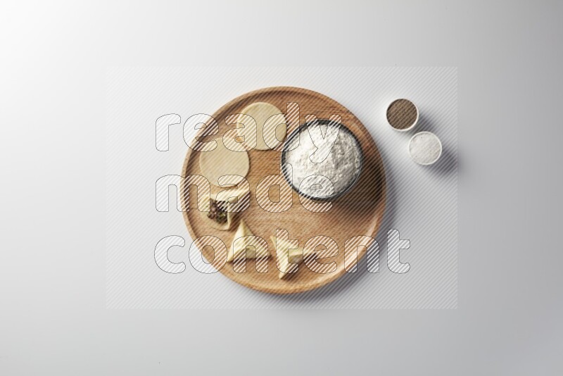 two closed sambosas and one open sambosa filled with meat while flour, salt, and black pepper aside in a wooden dish on a white background