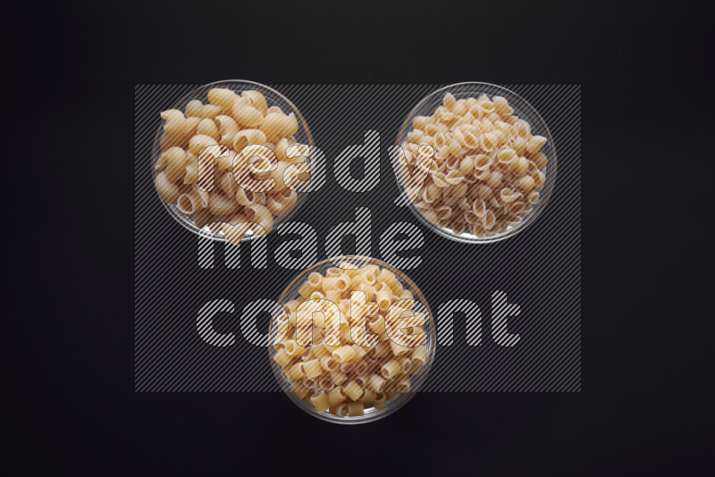 Different pasta types in glass bowls on black background