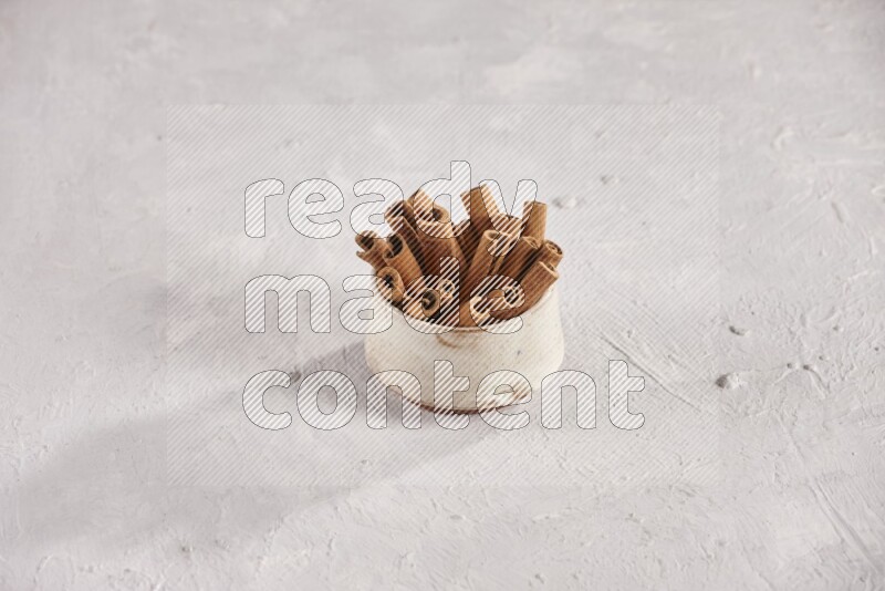 Cinnamon sticks in a beige bowl and more sticks beside it on white background