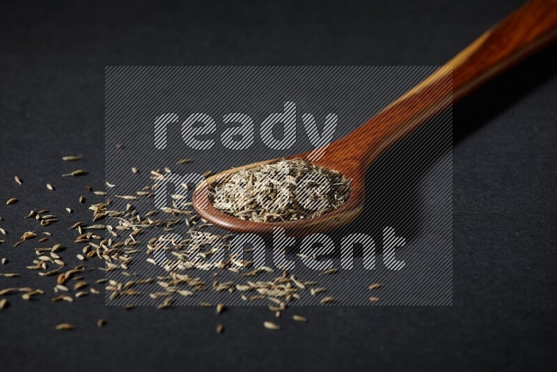 A wooden ladle full of cumin seeds on black flooring