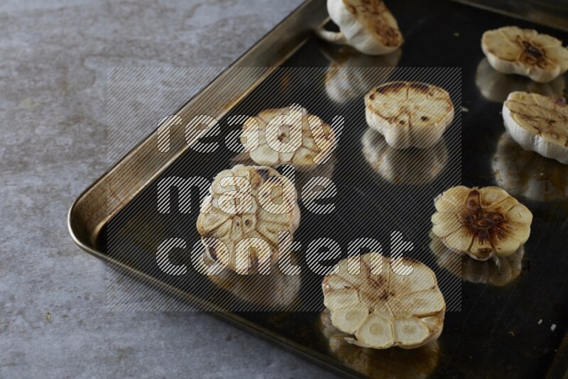 half's roasted garlic in a stainless tray on a grey textured countertop