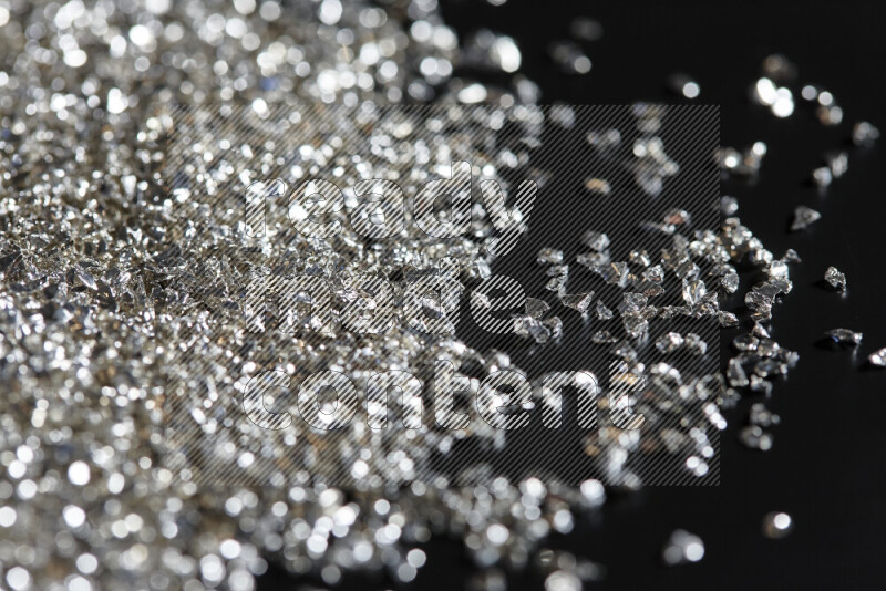 Silver shimmering fragments of glass scattered on a black background