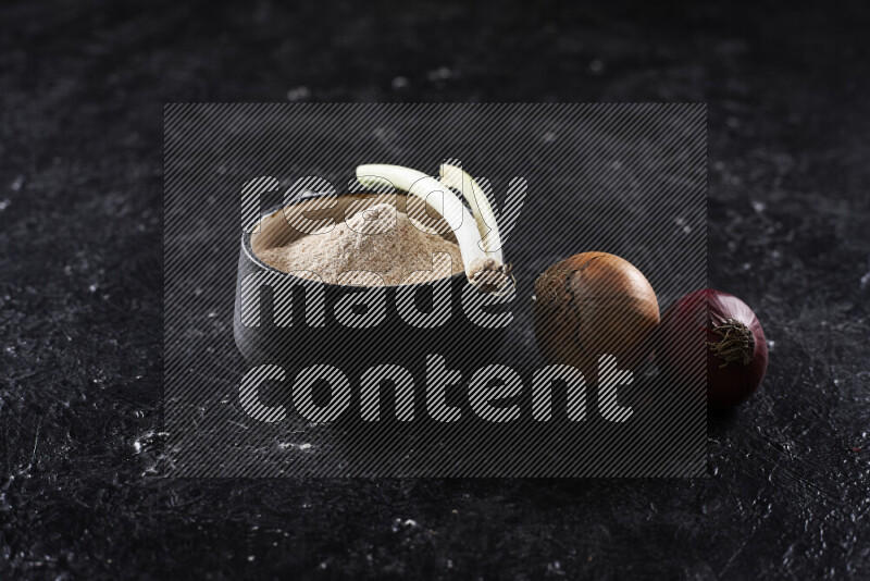 A black pottery bowl full of onion powder on black background