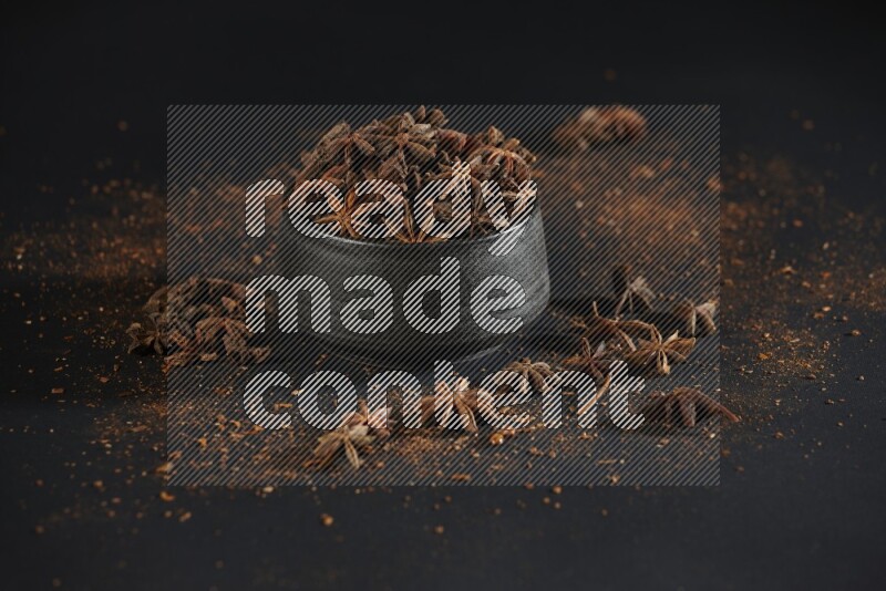 Star Anise in a black bowl with sprinkled anise on black flooring