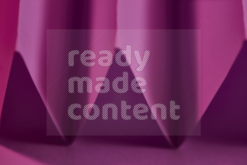 A close-up abstract image showing sharp geometric paper folds in pink gradients