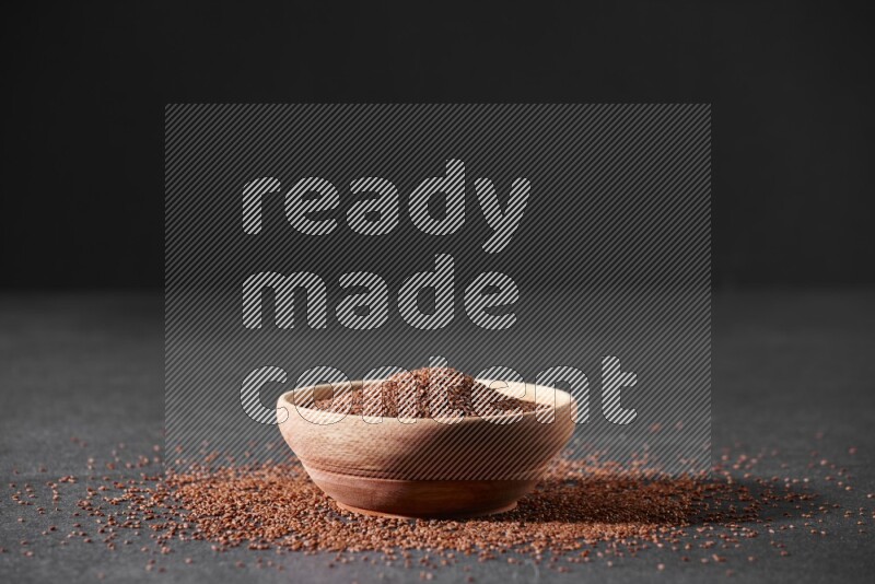A wooden bowl full of garden cress seeds surrounded by seeds on a black flooring