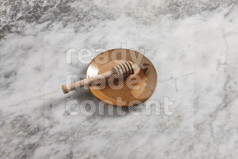 Multicolored pottery plate with wooden honey dipper in it on grey marble background