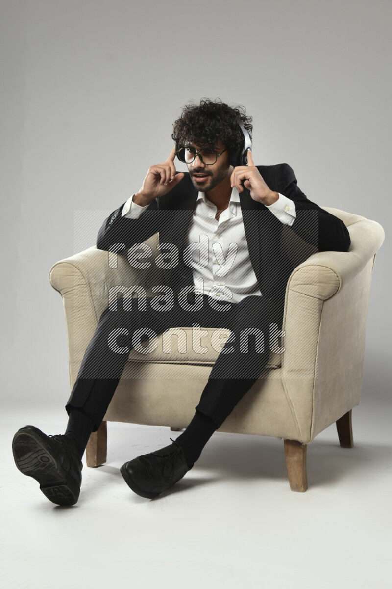 A man wearing formal sitting on a chair putting on headphones on white background