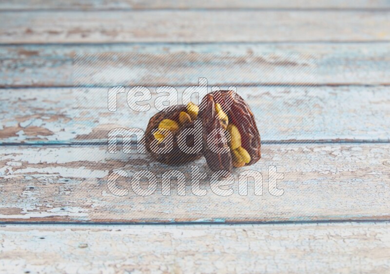 two pistachio stuffed madjoul dates on a light blue wooden background