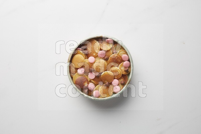 Top-view shot of mixed chocolate chips cereal pancakes in a round bowl on white background