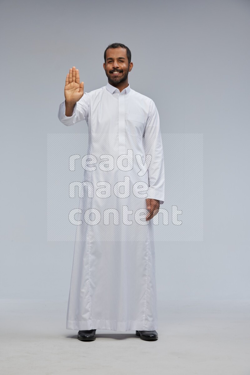 Saudi man Wearing Thob standing interacting with the camera on Gray background
