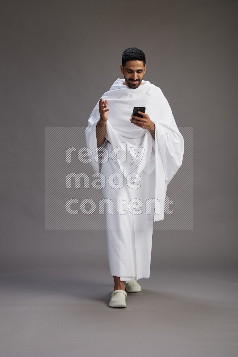 A man wearing Ehram Standing texting on phone on gray background